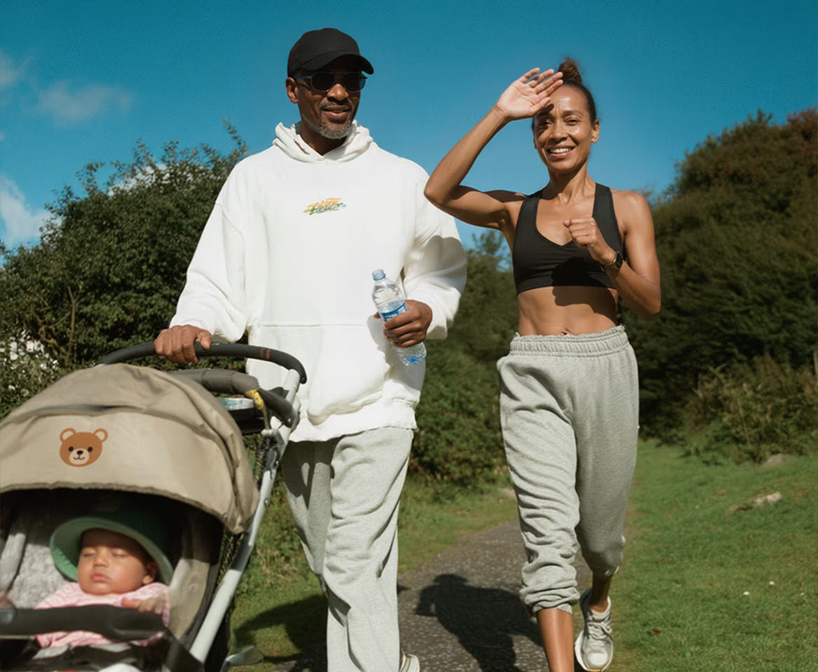 Man pushing a stroller with a baby, woman running in the park